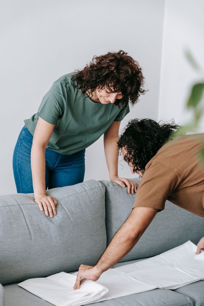 home-img A couple getting the living room ready by draping the couch with a white protective cover.